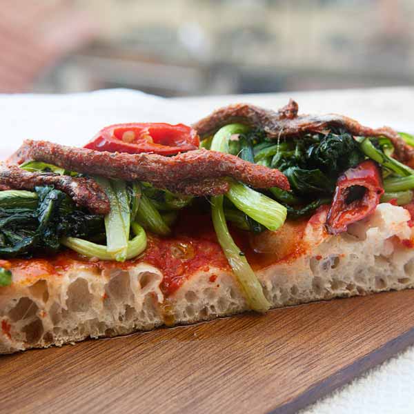 Pizza en tranches aux tomates, olives, anchois et roquette